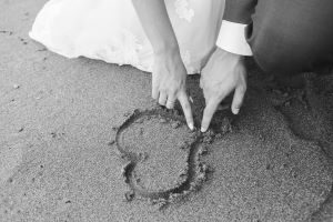 Photo of a wedding couple making a heart in the sand at a beach wedding